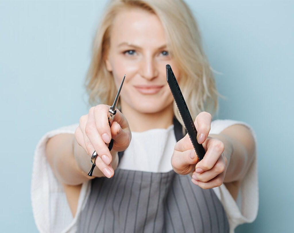 Junge Frau vor einer blauen Wand hält Schere und Kamm in die Kamera bei einer Business Selfie Shooting