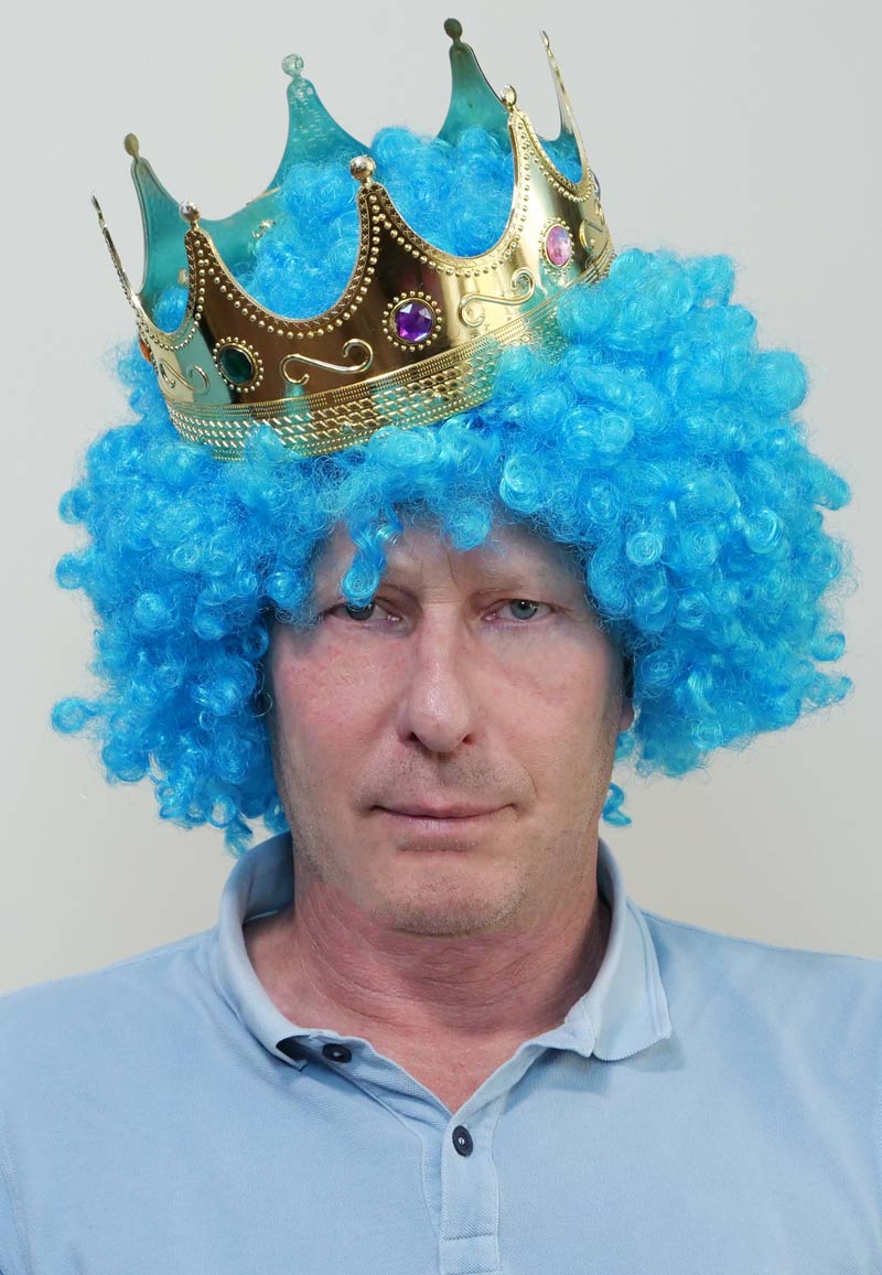 Lustiger Mann im Selfie Fotostudio mit blauer Lockenperücke und Krone