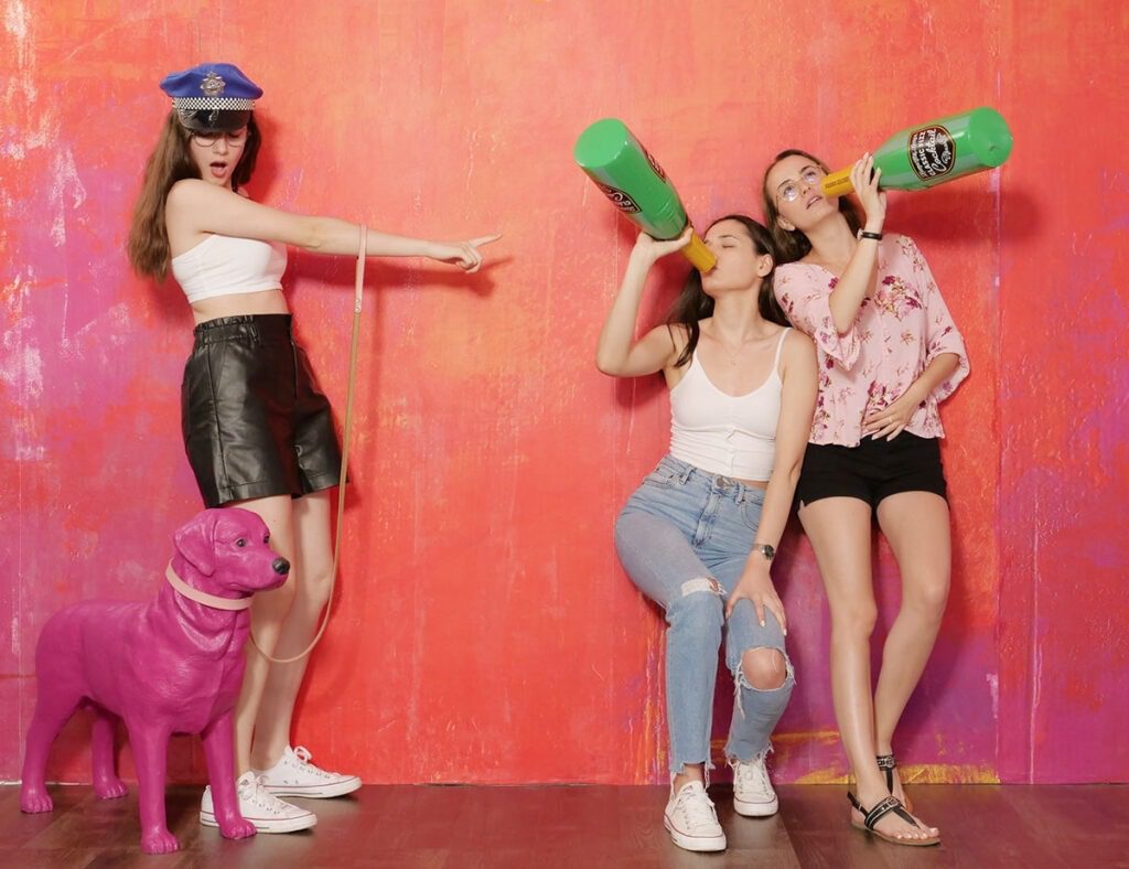 Drei junge Frauen machen Spass beim Teens Birthday Party im Selfie Fotostudio vor einer roten Wand mit Hund und Sektflaschen