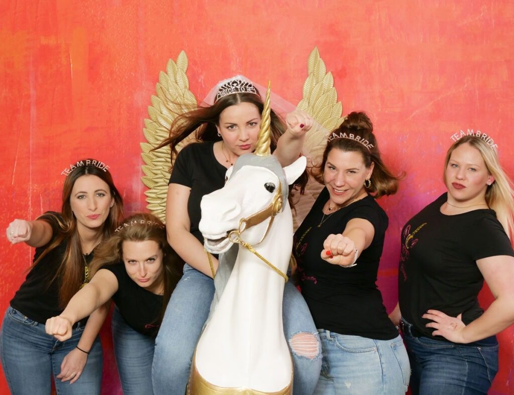 Braut mit ihrer lustigen Crew reitet auf einem Einhorn beim JGA Fotoshooting