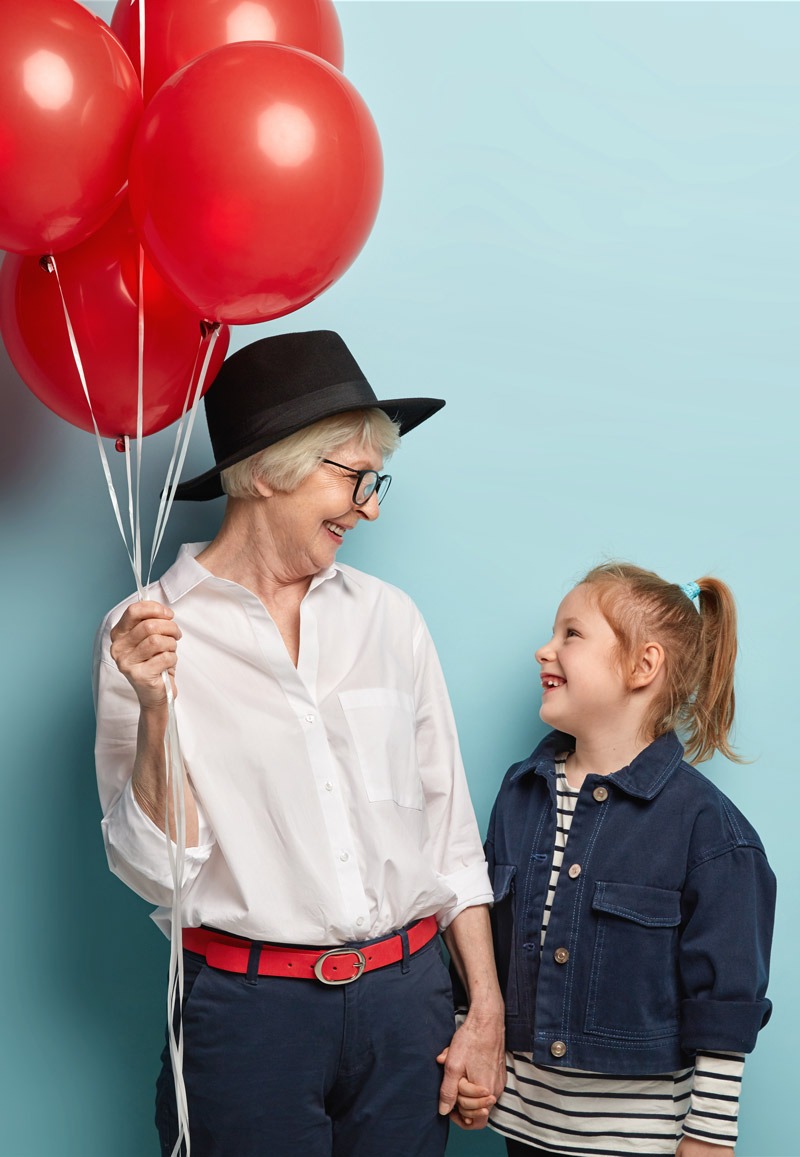 Fröhliche Oma mit Enkelin im Selfie Fotostudio vor einer blauen Wand mit roten Luftballons